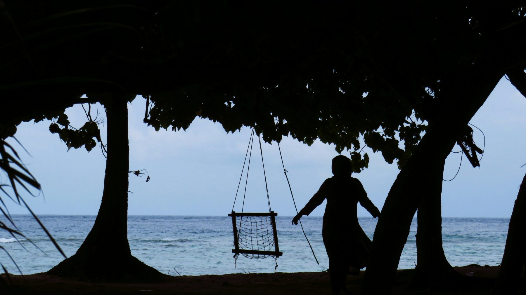 Silhouette of a local woman by the beach swing at sunset on Fulidhoo Island, Maldives